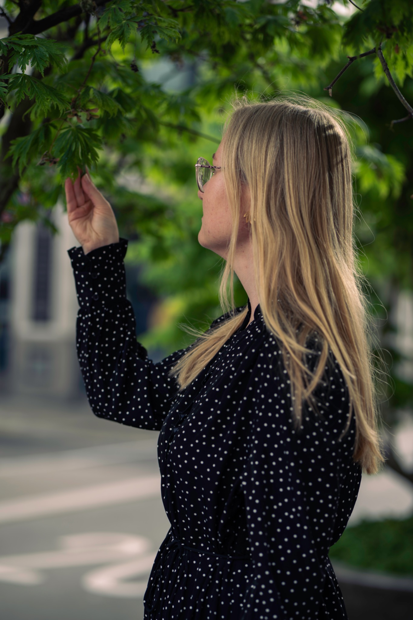 Blonde woman in glasses touching green leaves
