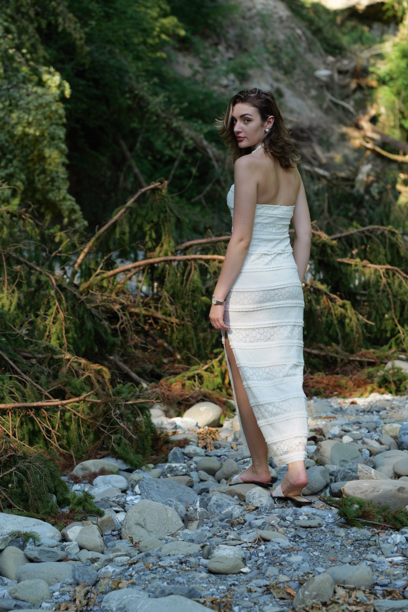 Woman in a white dress looking back at the camera in a rocky riverbed