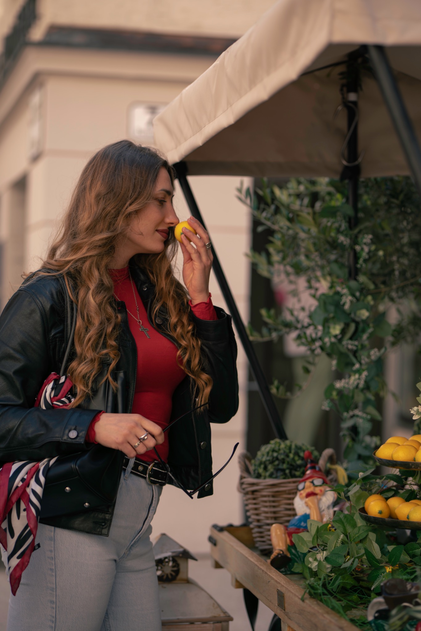 Woman in a leather jacket smelling a lemon beside a plant stand